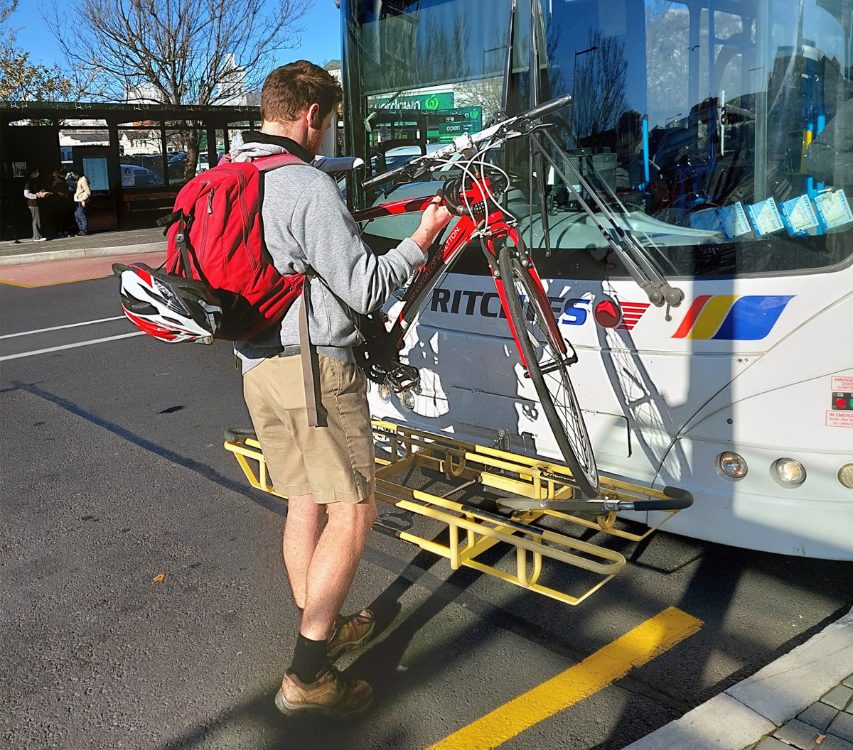 Bike being loaded onto bike rake on front of Ritches bus in Dunedin octagon bus stop